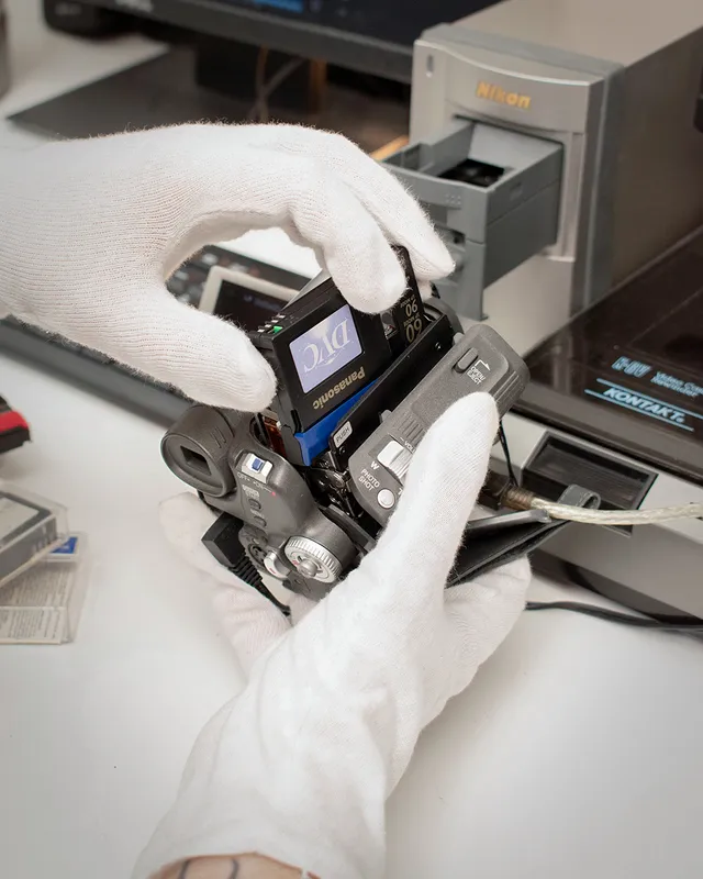 Técnico insertando una cinta MiniDV en una videocámara junto al escáner Nikon