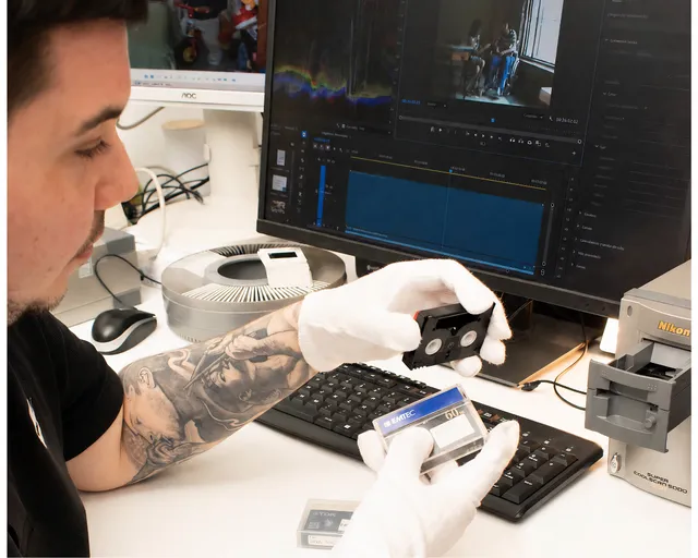 Técnico examinando cintas MiniDV frente al monitor de edición de vídeo