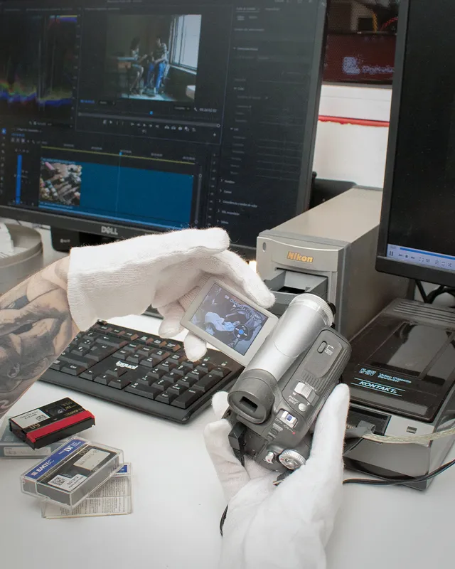 Técnico revisando el visor de una videocámara MiniDV frente al ordenador de edición